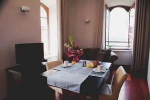 A dining area with a table set for two, a television on a stand, and a window with curtains. - Appartement 3 étoiles - ccbefb0 (Saint-Lizier)