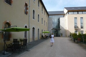 A courtyard with outdoor seating and a building entrance. - Appartement 3 étoiles - ccbefb0 (Saint-Lizier)