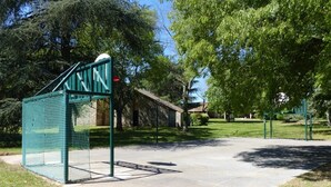 Ein Fußballplatz aus Beton mit Tor und Netz, umgeben von Bäumen und einem Gebäude im Hintergrund.