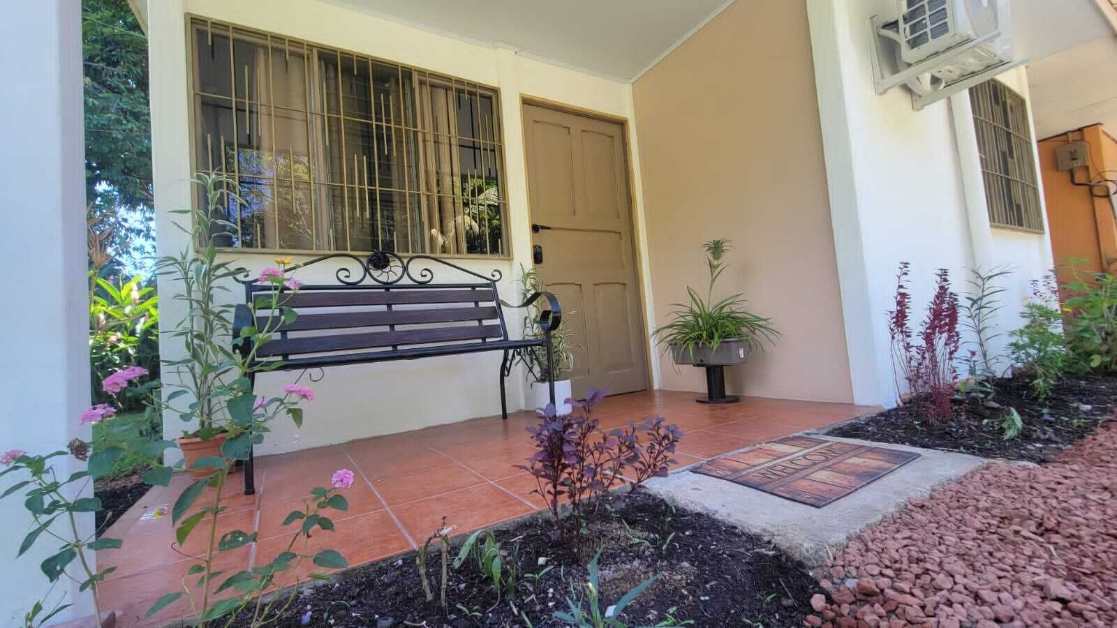A patio with a bench, potted plants, and a tiled floor.