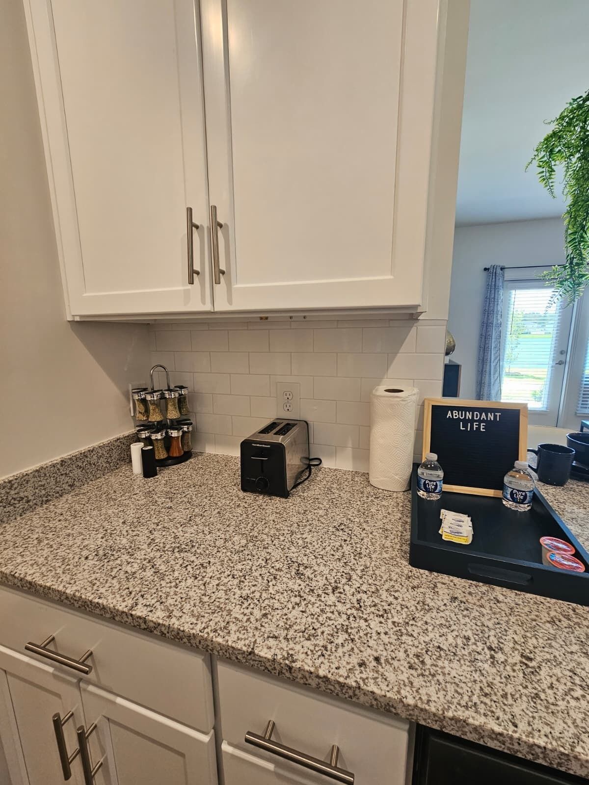 Eine Küche mit weißen Schränken, einer Granit Arbeitsplatte, einem Toaster, einer Kaffeemaschine und einem Schild mit der Aufschrift 'ABUNDANT LIFE'.