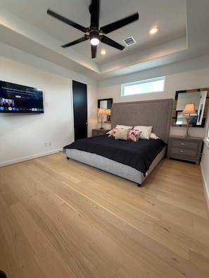 Ein Schlafzimmer mit Bett, Deckenventilator, Fernseher, Fenster, Spiegel und Nachttisch.
