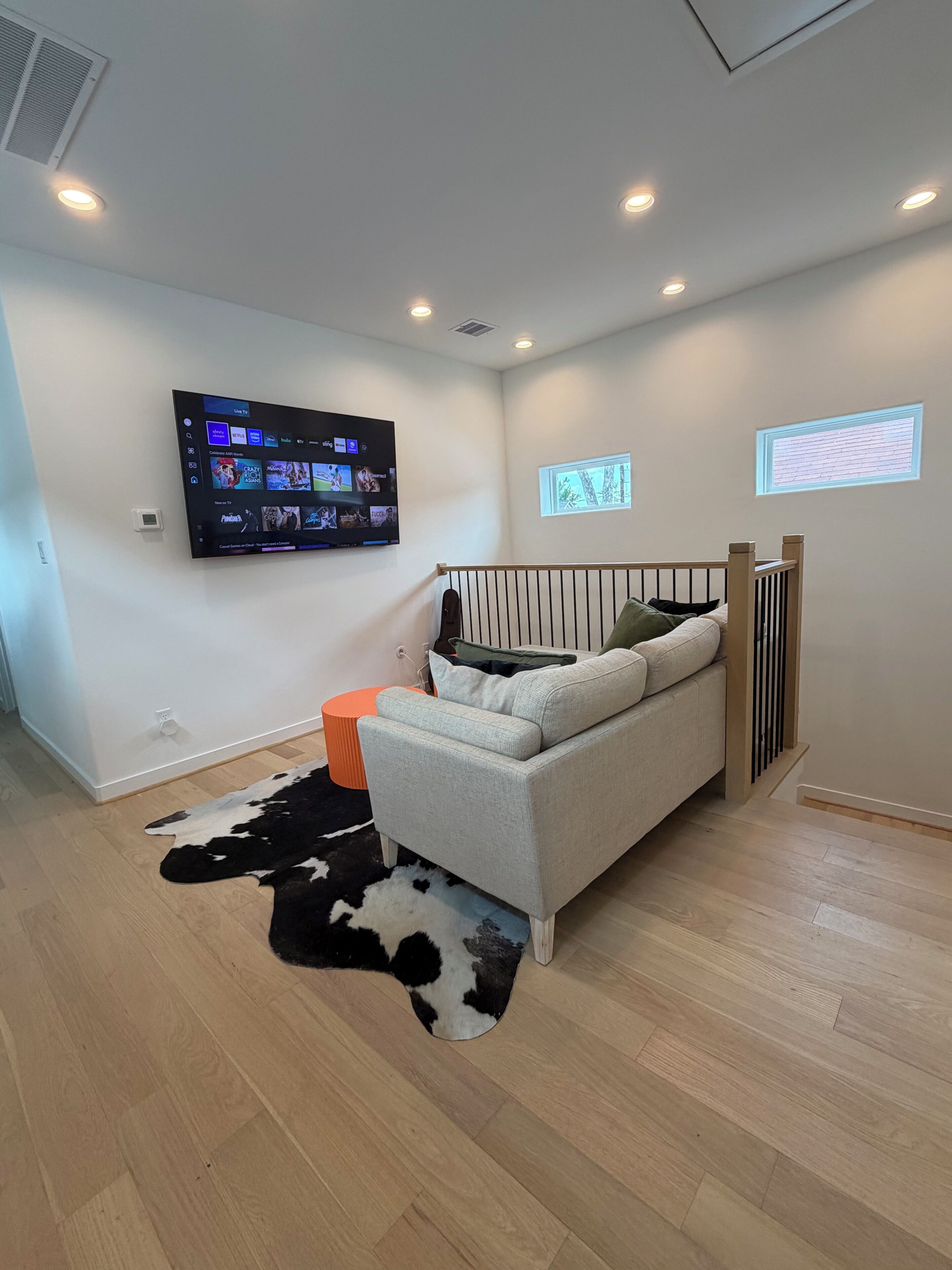 Una sala de estar moderna con un televisor montado, un sofá, suelo de madera y una ventana con persianas.