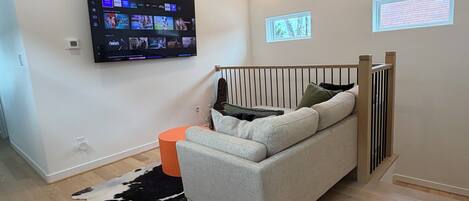 Una sala de estar moderna con un televisor montado, un sofá, suelo de madera y una ventana con persianas.