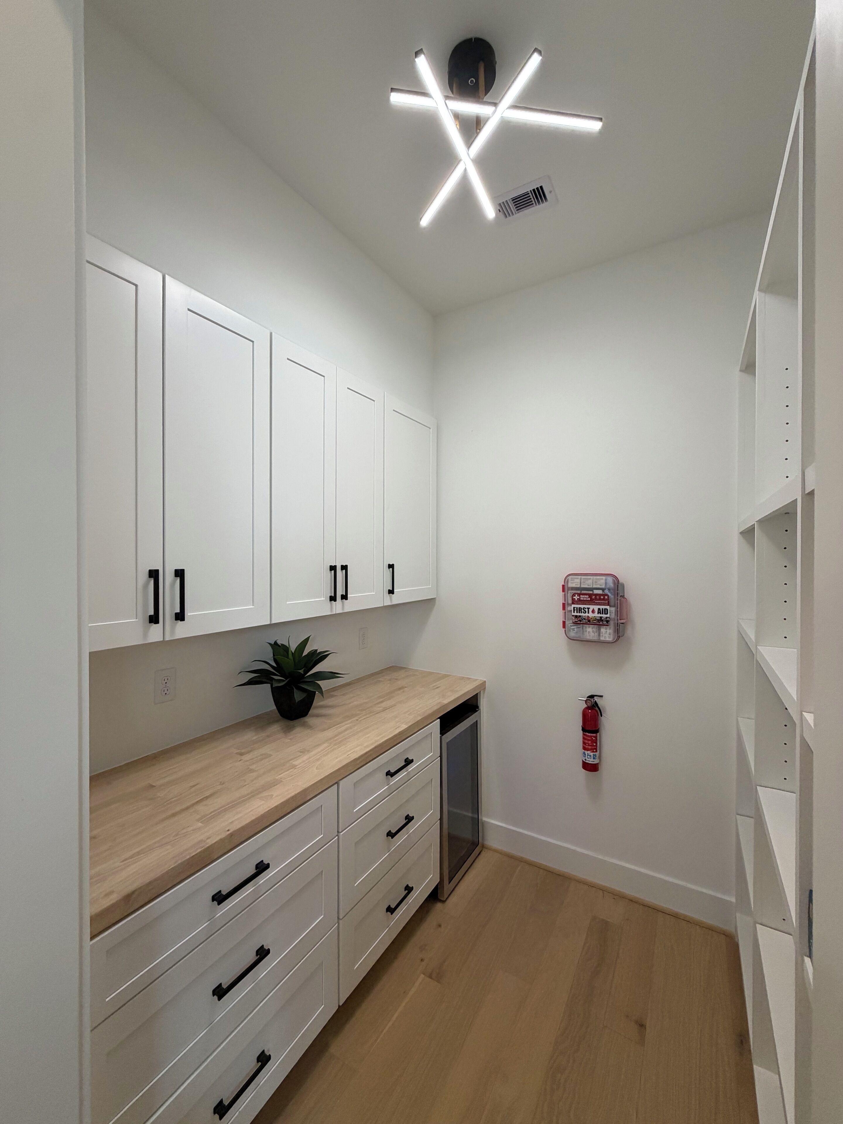 A modern kitchen with white cabinets, a wooden countertop, and a ceiling light fixture.