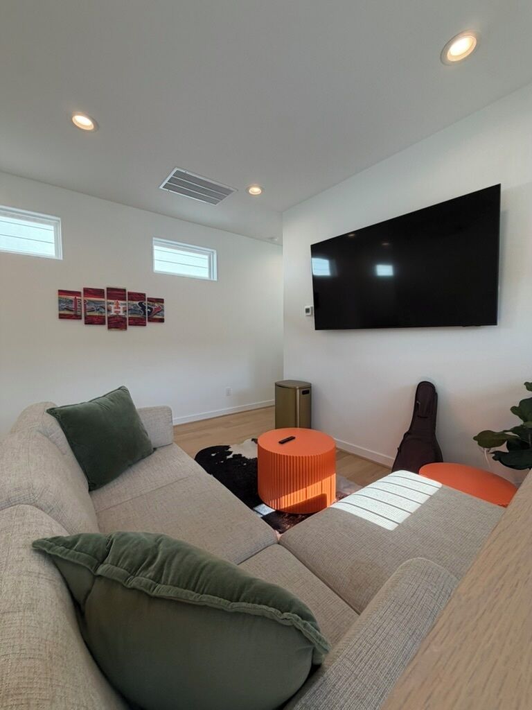 En moderne stue med en modulsofa, et fladskærms-tv, en guitar og en lille orange skammel.