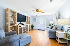 Ein Wohnzimmer mit einer Couch, einem Fernseher, Holzregalen und einem Deckenventilator.