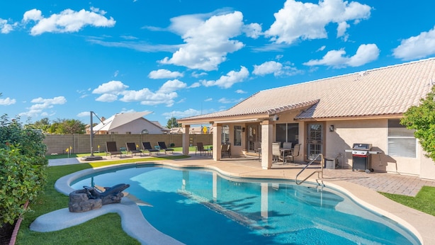 Ein Swimmingpool mit Liegestühlen, eine überdachte Terrasse und ein Gebäude mit einem Ziegeldach.