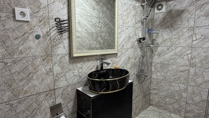 A bathroom with a marble wall, a black sink with gold trim, a mirror, and a shower area. - Valeria Homes Sultanahmet (fatih)