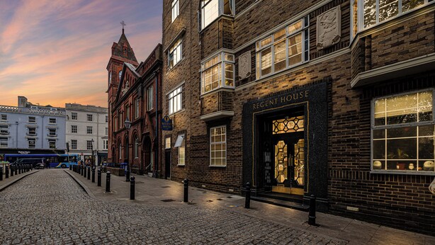 Una calle empedrada con edificios históricos, incluyendo una casa de estilo regencia con una entrada destacada.