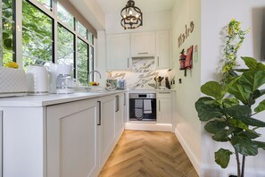 Una cocina moderna con armarios blancos, horno integrado y suelo de madera en patrón de espiga.