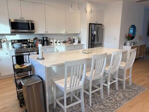 Une cuisine moderne avec des meubles blancs, des appareils en acier inoxydable, un îlot central doté de chaises et un tapis à motifs.