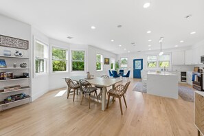 A spacious kitchen with white cabinetry, a central island, and a dining area with a table and chairs. - Long Island Waterfront Escape w/ Private Dock (Center Moriches)