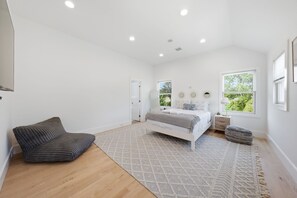 Un dormitorio amplio con una cama grande, una zona de estar con una silla y un ventanal con vistas a zonas verdes.