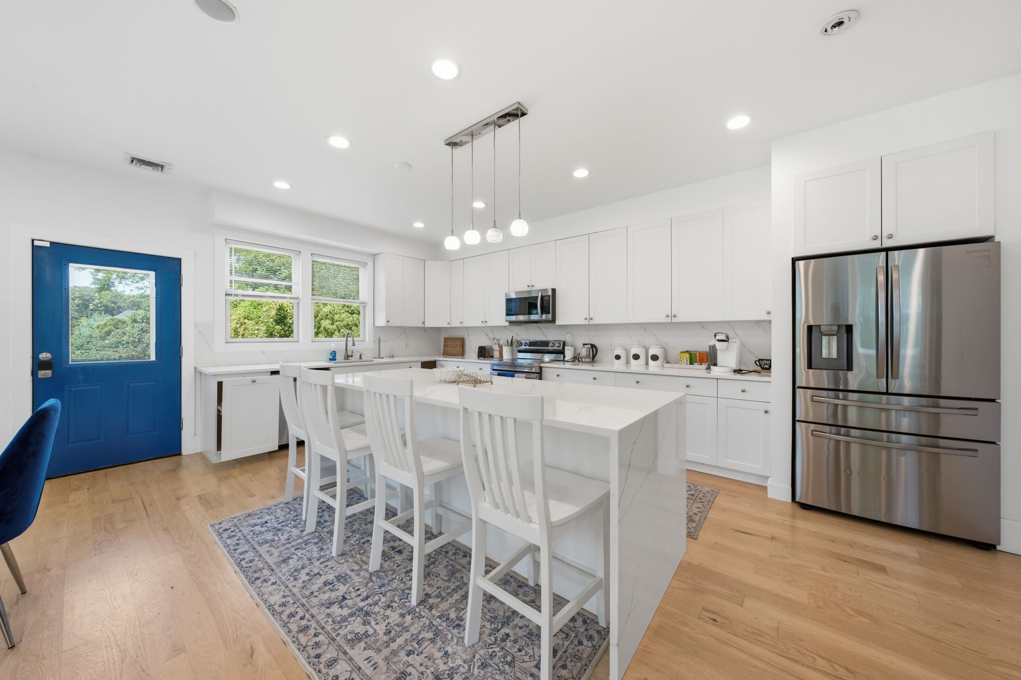 A modern kitchen with white cabinetry, stainless steel appliances, and a central island with bar stools.