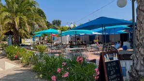 Um café ao ar livre com guarda-sóis azuis, mesas na área externa e um cardápio em lousa.