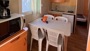 Cozinha compacta com mesa de jantar, cadeiras, micro-ondas e um pequeno frigorífico.