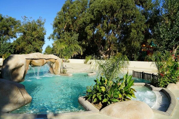 A swimming pool with a waterfall feature, surrounded by lush greenery and trees.