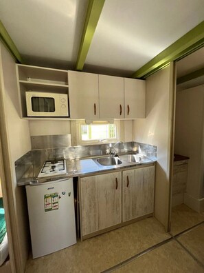 Une cuisine compacte équipée d’une cuisinière à gaz, d’un four à micro-ondes, d’un évier et de meubles de rangement en bois.