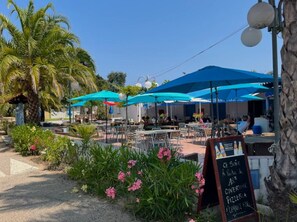 An outdoor cafe with blue umbrellas, outdoor seating, and a chalkboard menu.