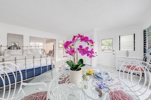 Une chambre moderne avec un lit, une table à manger et des chaises, une plante en pot et une fenêtre avec des stores.