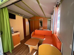 A compact living space with a sofa, a small table, a kitchenette, and a window with curtains.