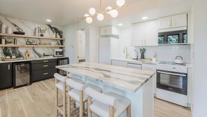 Une cuisine moderne dotée d’un îlot en marbre, de tabourets de bar, d’appareils électroménagers intégrés et d’un luminaire au plafond au design original.