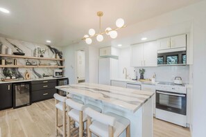 A modern kitchen with a marble island, bar stools, built-in appliances, and a unique ceiling light fixture. - 1BR Condo, Pool & Hot Tub, fitness center, trails (Bend)