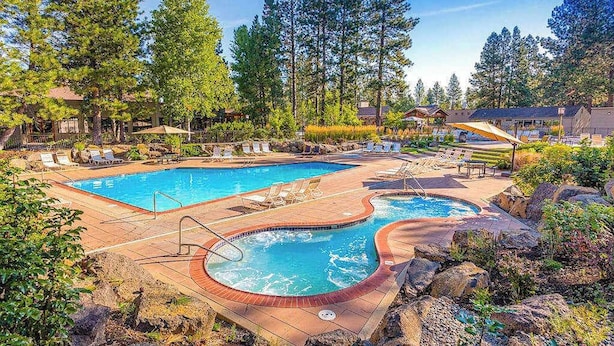Un espace piscine comprenant deux piscines, des chaises longues et une terrasse en bois.
