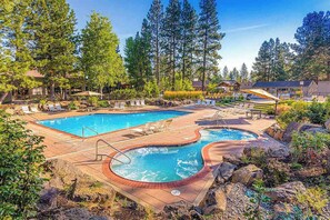 Un espace piscine comprenant deux piscines, des chaises longues et une terrasse en bois.