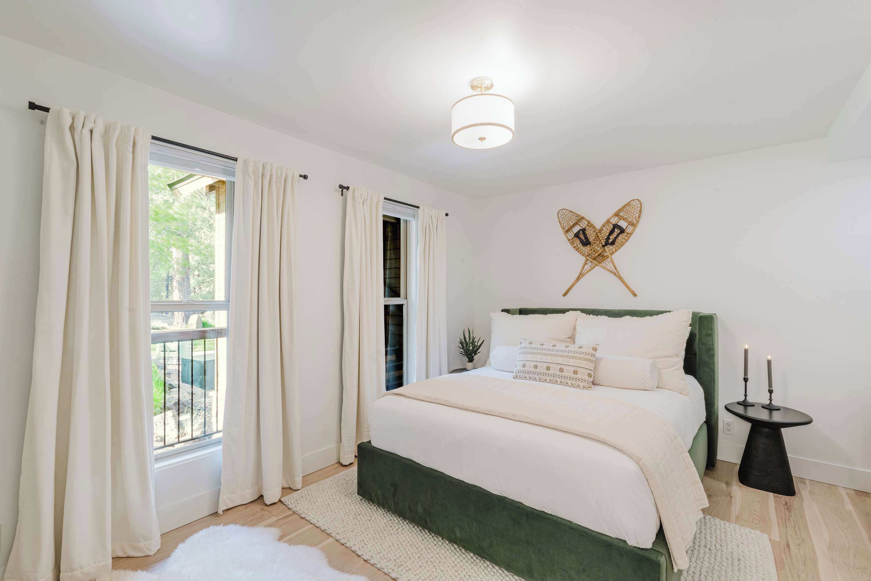 Un dormitorio con cama, cortinas, una lámpara de pared y una mesita con velas.
