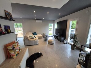 Un salon moderne avec un canapé, un pouf, une télévision et un chien allongé sur le sol.