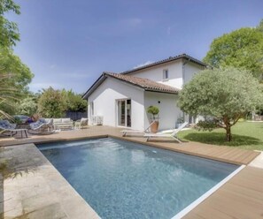 Une maison avec une piscine, une terrasse dotée de chaises longues et un petit jardin.