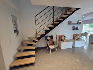 Un intérieur moderne avec un escalier en bois, une chaise et une table agrémentée de coussins.