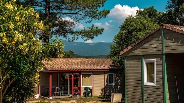 A small wooden house with a tiled roof, a covered porch, and a view of mountains in the background. - Chalet 2 étoiles - Piscine  - ccbgdfh (Porto-Vecchio)