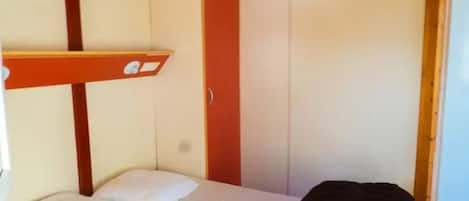 Una cama litera con estructura roja, una cama individual con ropa de cama blanca y un bolso negro en el suelo.