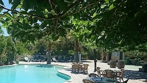 A pool area with a wooden deck, lounge chairs, and tables. - Chalet 2 étoiles - Piscine  - ccbgdfh (Porto-Vecchio)