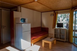 Ein kompakter Raum mit einer Küchenzeile, einem roten Sofa, einem kleinen Holztisch und einem Fernseher auf einem Schrank.