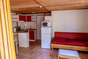 Une pièce compacte comprenant un coin cuisine, un four à micro-ondes, un réfrigérateur, un canapé rouge et une petite table.