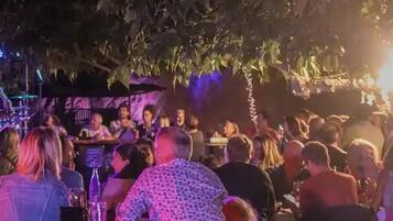 Un espacio al aire libre con mesas y sillas lleno de gente, rodeado de follaje.