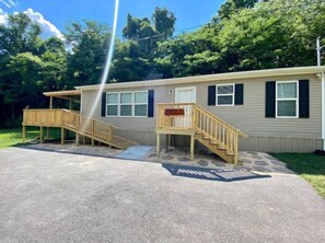 A single-story mobile home with a front porch, a small deck, and a driveway. - Mountain Air #2438 (Pigeon Forge)