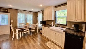 A kitchen with wooden cabinets, a dining table with chairs, a window with curtains, and a sink. - Mountain Air #2438 (Pigeon Forge)