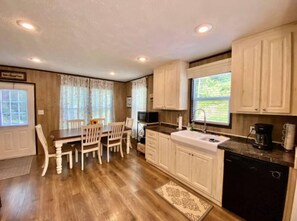 A kitchen with wooden cabinets, a dining table with chairs, a window with curtains, and a sink. - Mountain Air #2438 (Pigeon Forge)