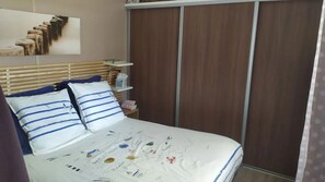 A bedroom with a bed, a wooden headboard, a nightstand with a lamp, and a wardrobe. - Chalet 4 étoiles - Piscine  - ccbfgd0 (Saint-Hilaire-de-Riez)