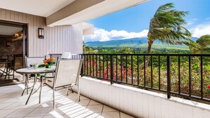 A balcony with a table and chairs, a view of a landscape with mountains and palm trees. - Kaanapali Alii-1 Bedroom Garden/Mountain Views (Lahaina)