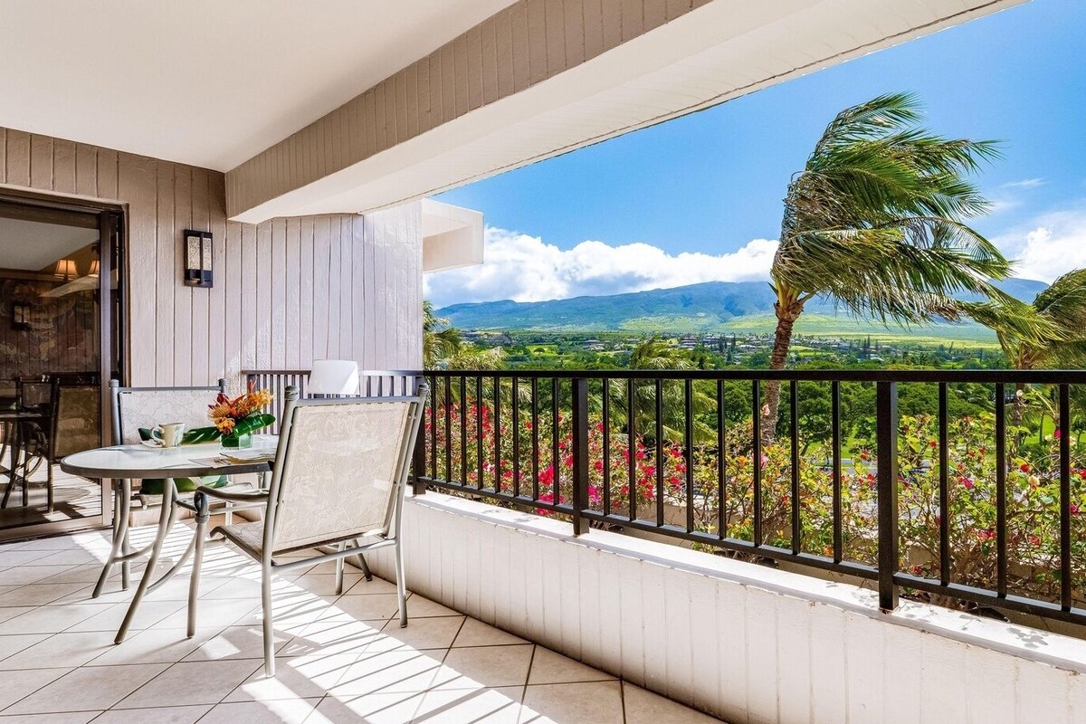 A balcony with a table and chairs, a view of a landscape with mountains and palm trees.