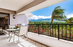 A balcony with a table and chairs, a view of a landscape with mountains and palm trees. - Kaanapali Alii-1 Bedroom Garden/Mountain Views (Lahaina)