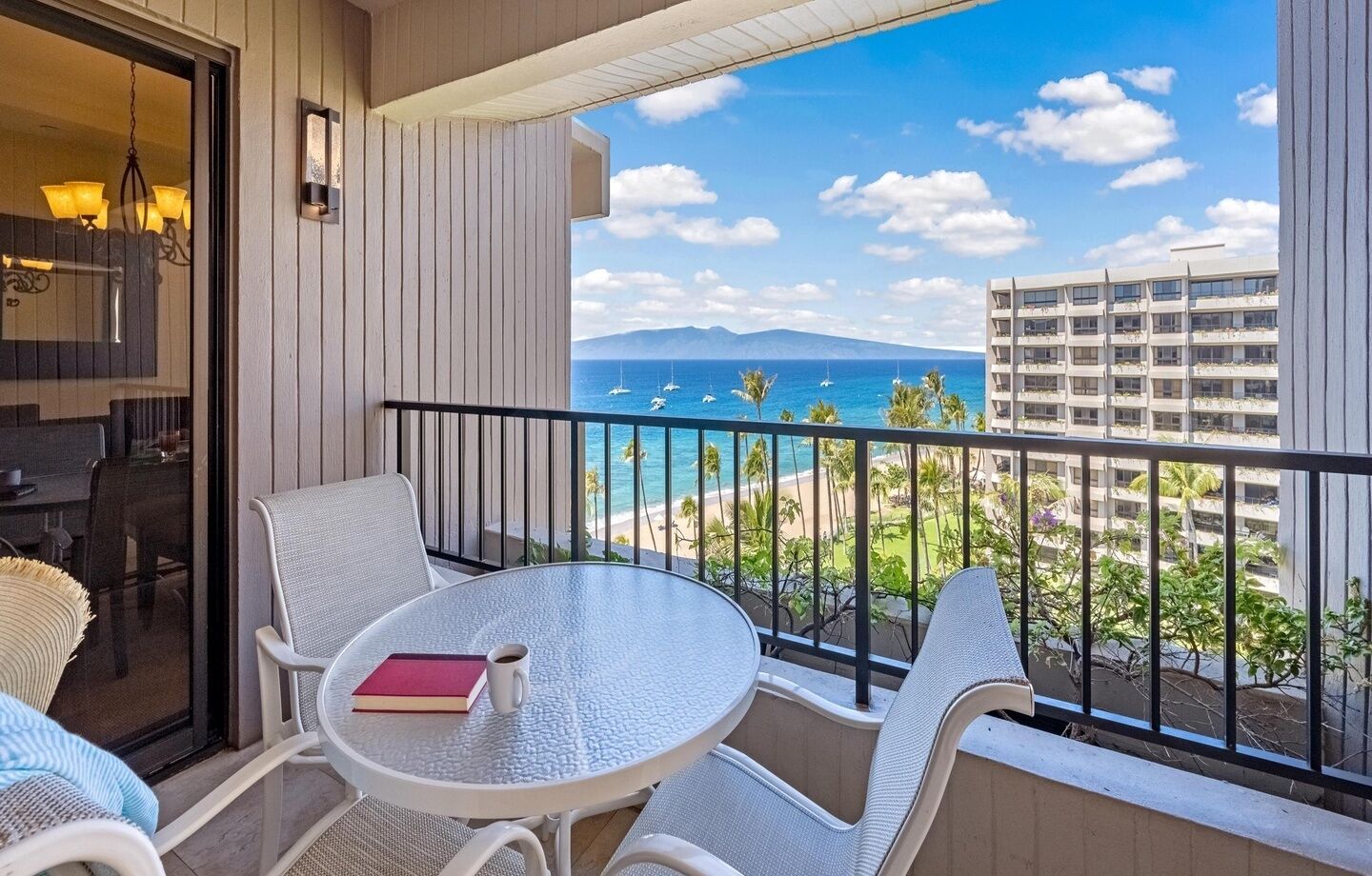 A balcony with a table and chairs, a view of the ocean, and a building in the background.