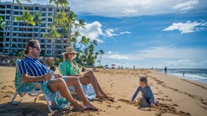 A beach scene with a hotel in the background, palm trees, and people on the sand. - Kaanapali Alii-1 Bedroom Ocean Views (Lahaina)