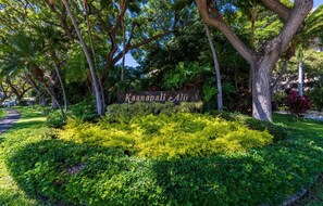 A sign with 'Kaanapali Ali' in the center of a well-maintained garden with various trees and shrubs.